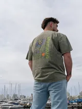 Remera oversize verde con efecto acid wash, mangas cortas y estampa gráfica en la espalda con diseño de flor de mburucuyá y texto.
