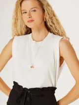 Camiseta sin mangas color blanco roto, con cuello redondo y hombros ligeramente caídos, de corte recto y ajustado al cuerpo.