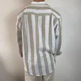 Camisa de manga larga con cuello mao, confeccionada en tejido de lino a rayas verticales en tonos blanco y celeste. Presenta cierre frontal con botones y corte clásico.