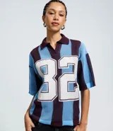 Remera de punto con diseño sportcore, cuello polo y mangas cortas amplias. Presenta un patrón de rayas verticales en tonos azul y bordó, con el número 82 estampado en el frente.