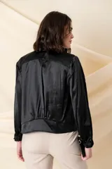 Campera tipo bomber color negro, confeccionada en tejido satinado. Presenta cierre frontal metálico, bolsillos laterales con hebillas decorativas doradas y puños elásticos.
