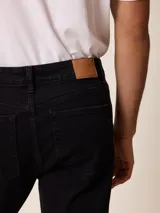 Jean de corte recto y tiro medio, confeccionado en denim de color negro con costuras a tono. Cuenta con cierre frontal con botón metálico, cinco bolsillos tradicionales y pasacintos en la cintura.