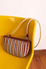 Cartera de cuero trenzado a mano, con diseño de rayas verticales en tonos bordó, amarillo y blanco. Tiene una correa trenzada en amarillo y blanco, y herrajes dorados.