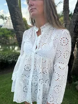 Camisa blanca de broderie con cuello mao, mangas largas amplias y cierre frontal con botones.