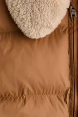 Chaleco acolchado de color tostado con diseño guateado, cuello de sherpa en tono crema, cierre frontal con cremallera y bolsillos frontales tipo parche.