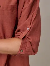 Camisa color beige de algodón y lino, con cuello clásico, cierre frontal con botones, mangas largas con puños abotonados, dos bolsillos con solapa en el pecho y corte holgado.