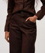 Pantalón de sarga color marrón con corte barrel, cintura media, cierre frontal con botón y cremallera, bolsillos funcionales y recortes estructurales en las piernas.