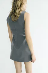 Vestido corto de corte recto y cuello redondo, sin mangas. Presenta un detalle de lazo decorativo en la cintura y cierre de cremallera oculta en la espalda.
