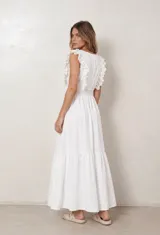 Vestido largo blanco de corte cruzado con escote en V, cintura fruncida elástica y mangas con volados de broderie. Presenta una falda larga con volado en el ruedo.