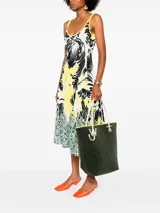 Bolso tipo tote de chenilla color verde oscuro con ribete amarillo. Tiene dos correas de hombro color crema, compartimento principal con bolsillos internos y apliques metálicos con el logo de la marca.