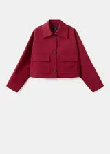 Chaqueta corta de algodón en color rojo, con cuello camisero, manga larga y cierre frontal de botones oscuros. Presenta dos bolsillos con solapa en el frente.