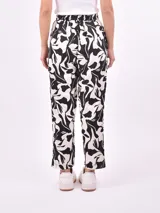 Pantalón babucha de tiro alto con cintura fruncida y lazo para ajustar. Estampado de hojas tropicales en tonos naranja y marrón sobre fondo blanco.