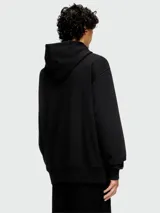 Buzo negro con capucha de corte holgado, con logo metálico en el pecho y bolsillo tipo canguro.