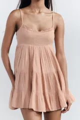 Vestido corto negro de gasa con escote recto y tirantes finos ajustables. El corpiño tiene fruncido elástico y el ruedo es escalonado con volados. Presenta un detalle de encaje a tono en el borde del escote.