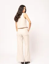 Pantalón de lino color beige, de tiro alto, pierna ancha y levemente acampanada. Tiene pinzas delanteras, elástico en la pretina trasera, cierre delantero y broche interno, bolsillos laterales y dobladillo invisible.