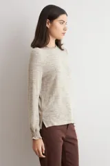 Remera de manga larga con cuello alto tipo media polera, confeccionada en tejido texturado de color beige melange, con puños con detalle de volados.