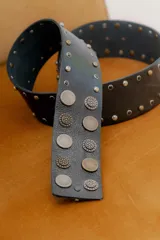 Faja de cuero color tostado con diseño de tachas metálicas circulares grabadas y cierre frontal con hebilla.