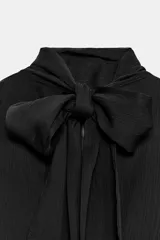 Blusa sin mangas blanca con estampado de lunares negros, cuello alto drapeado y nudo frontal en el bajo.