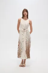 Vestido largo sin mangas, color crudo, con estampado de hojas en tonos marrones y negros. Presenta un cuello redondo y un lazo de tela a juego que ajusta la cintura. La falda es fluida y tiene aberturas laterales.