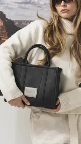 Cartera estructurada de tamaño mediano, confeccionada en símil cuero color negro. Presenta doble asa de mano, correa larga ajustable y desmontable, y un bolsillo trasero con cierre. El compartimento principal cuenta con cierre, división interna y bolsillos organizadores.