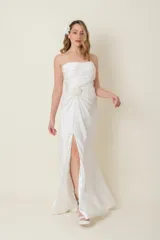 Vestido largo blanco de satén de seda natural, con breteles finos, escote recto, drapeado en el busto, tajo lateral y cola corta. Presenta aplique de flor de organza bordada en un costado.