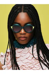 Lentes de sol Tiwi modelo Kora, con armazón redondo de acetato en color verde traslúcido y detalles triangulares en color amarillo en los extremos. Lentes oscuros con protección UV.