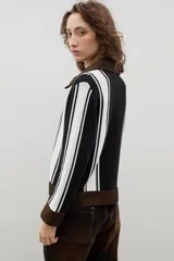 Campera de estilo casual confeccionada en una combinación de tejido de punto a rayas verticales en blanco y negro, con detalles en denim marrón en cuello, puños, ruedo y cierre frontal.