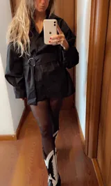 Camisa vestido negra con mangas largas abullonadas, cuello camisero, cierre frontal con botones y cinturón con hebilla metálica. Se usa con medias de lycra negras y botas texanas de cuero negras con apliques blancos.