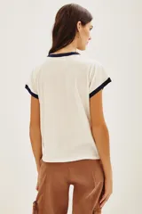 Remera de algodón color crema con cuello y bordes de mangas en contraste azul marino. Presenta un diseño frontal con bordados de flores coloridas y la inscripción 'MARCHÉ aux FLEURS' en letras azules.