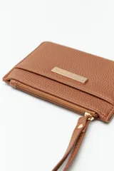 Billetera color mostaza con textura granulada, cierre superior con cremallera y correa de muñeca.