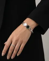 Esclava rígida de acero inoxidable con diseño de círculos entrelazados, presentando un círculo central con incrustación de nácar blanco y otro con ónix negro.