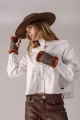 Camisa blanca de algodón con cuello alto, mangas largas abullonadas y cierre frontal de botones. Presenta un diseño delantero con alforzas y detalles de bordado inglés en forma de V.