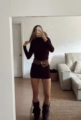 Vestido corto de manga larga en color bordó, con cuello alto y diseño ajustado con frunces laterales que recorren toda la prenda.