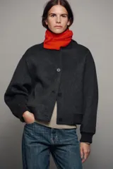 Cazadora bomber beige confeccionada en hilatura con lana, con cuello subido, manga larga y bolsillos frontales. Presenta cierre frontal con botones oscuros y puños, cuello y ruedo en tejido rib.