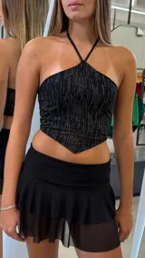 Top negro con escote halter y tiras finas cruzadas en el cuello. Presenta un estampado de líneas verticales brillantes y un corte asimétrico en el bajo, terminando en punta.