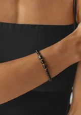 Pulsera de cristalitos facetados negros, intercalados con cuentas cilíndricas y detalles dorados.
