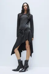 Vestido midi de cuello redondo y manga larga, confeccionado en tejido de punto gris oscuro. Presenta un cinturón integrado con hebilla y aplicación de tachas metálicas, y un bajo con diseño asimétrico y volados.