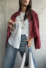 Camisa de lino color blanco, de corte holgado y manga larga con puños arremangados. Presenta cuello clásico, cierre frontal con botones y detalle de botones decorativos en el lateral inferior.