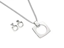 Set de joyería compuesto por un collar con dije cuadrado con centro circular y un par de aros tipo caravana a juego, ambos con diseño geométrico minimalista en acero pulido.