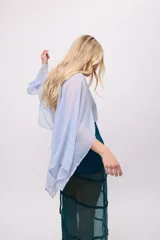 Poncho corto de chiffon color amarillo verdoso con textura plisada y brillo metálico. Presenta un cuello redondo y mangas amplias tipo capa.