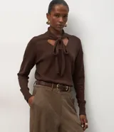 Suéter de punto color marrón chocolate, con mangas largas y diseño de cuello con recorte central y lazo ajustable.