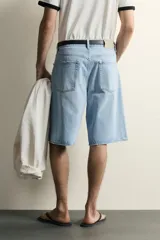 Bermuda de jean con corte holgado y pierna recta, confeccionada en denim de algodón rígido con efecto lavado. Presenta diseño clásico de cinco bolsillos y cierre frontal con botones.