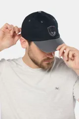 Gorro tipo gorra con visera de lona color azul, con parche tejido frontal que presenta diseño de paisaje y mar.