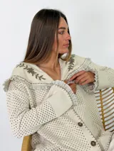 Saco de punto calado color beige, con cuello marinero grande adornado con bordados florales y volados en los bordes. Tiene mangas largas con puños anchos y cierre frontal de botones.