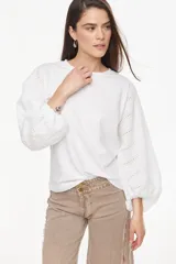 Blusa blanca de calce recto y relajado, con mangas largas abullonadas de broderie y puños ajustados.