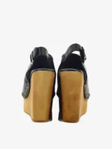 Sandalias de cuero negro con cuña alta de madera y plataforma delantera, detalle de tachas metálicas en los laterales y tira con hebilla en el talón.