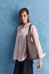 Camisa de calce relajado a rayas rosadas y blancas, con cuello camisero clásico y frente abotonado. Presenta recortes con cambio de dirección en las rayas y silueta amplia.