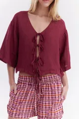 Blusa de lino italiano color beige, de manga corta, con escote en V y cierre frontal mediante lazos o moños.