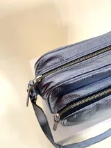 Bandolera rectangular de cuero azul metalizado con correa larga regulable. Cuenta con un bolsillo frontal con fuelle y un bolsillo trasero con cierre.