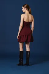 Vestido corto color bordó, con escote palabra de honor, diseño ajustado con frunces laterales y falda con volado en el ruedo.